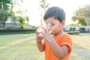 Boy drinks water with a glass in the garden