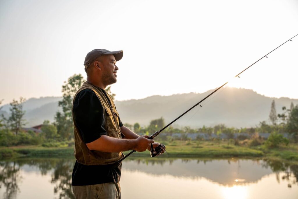 Excited emotion of Handsome fisherman fishing as a leisure activity during his vacation at the lake on sunset. Relax and hobby concept.