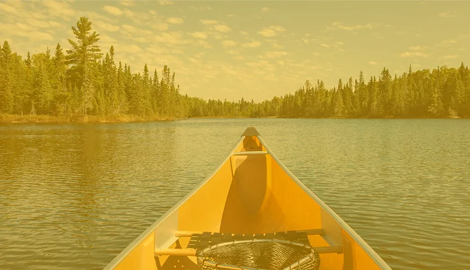Yellow canoe with fishing net on a blue lake with pines along the shore on a sunny summer afternoon in northern Minnesota